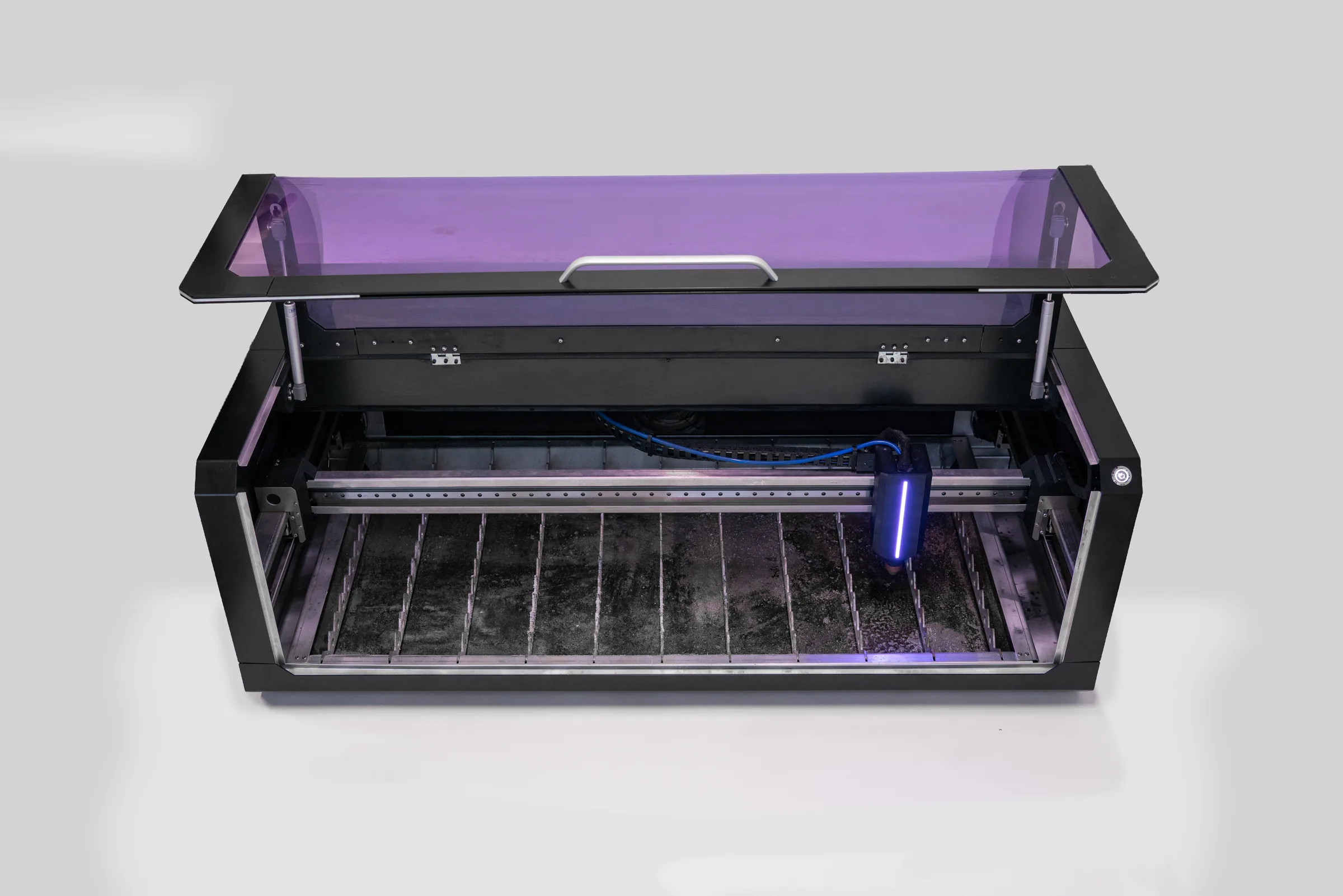 The Pilotarc desktop plasma CNC seen from the front with the tinted lid raised, showing the slat bed and the torch
