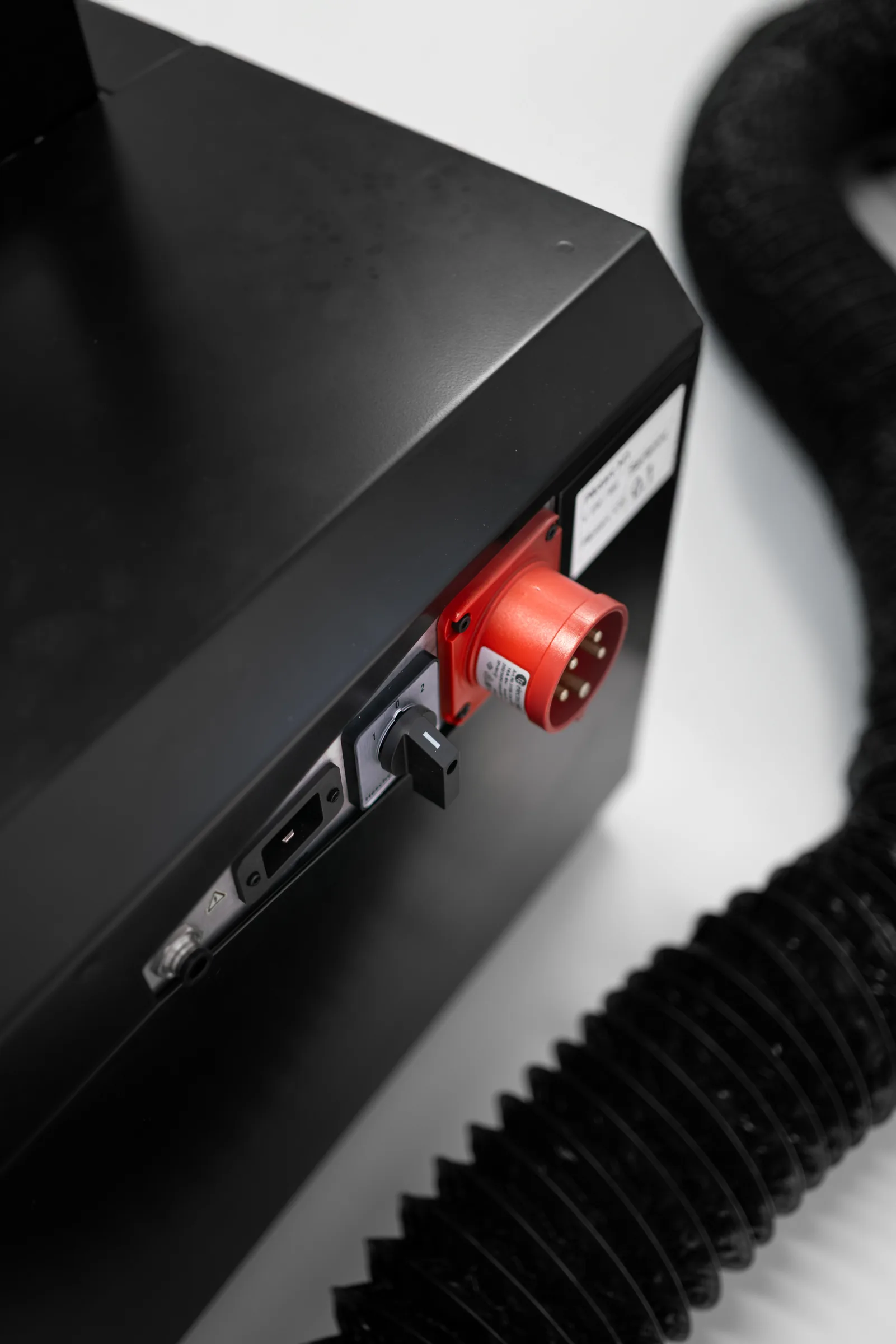 The rear corner of the machine: a red five-pin CEE inlet, a rotary isolator switch and the extraction hose