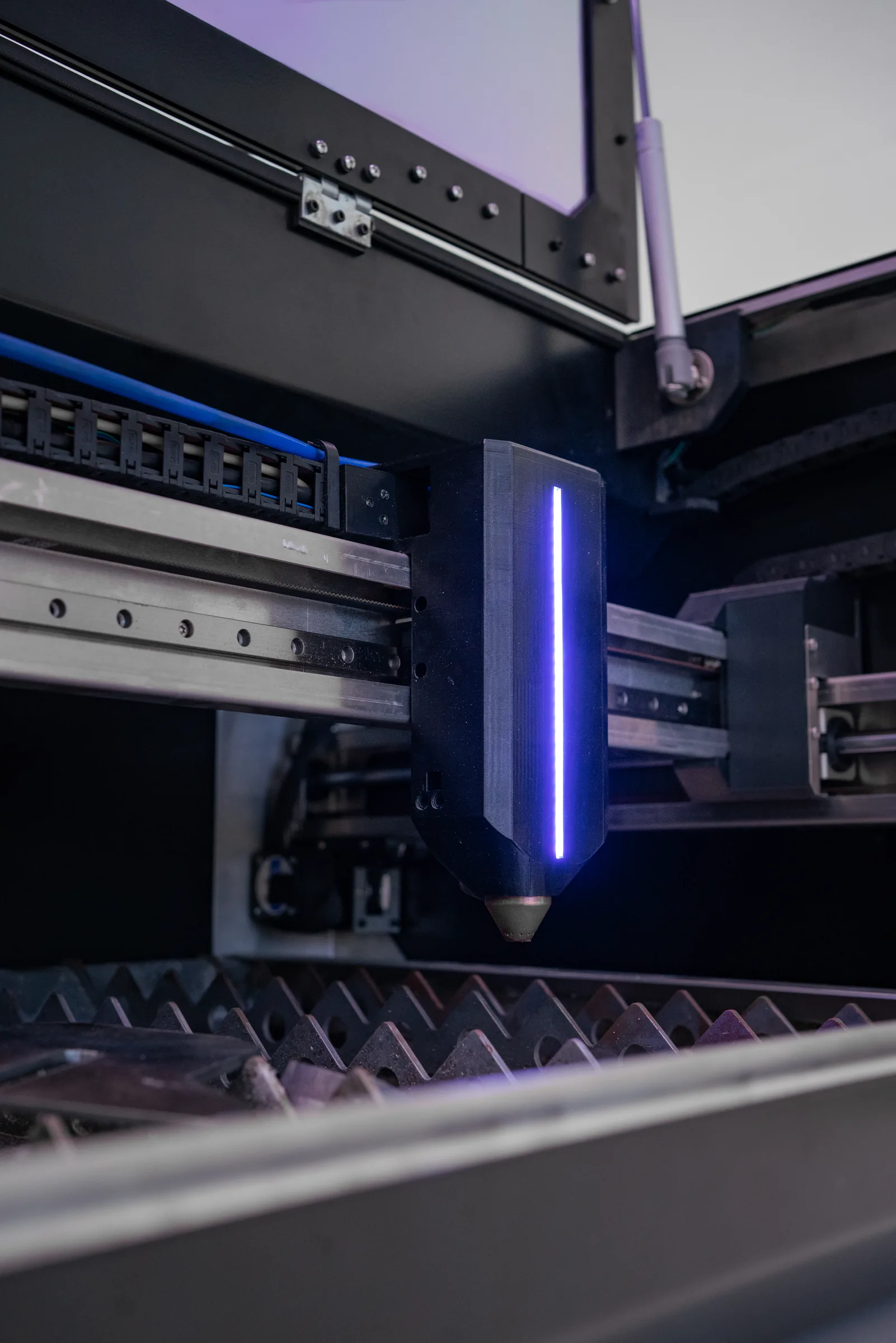 Close-up of the torch head on its linear rail, LED strip lit, above the slat bed